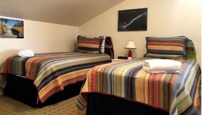 Quarto de hotel com duas camas, cada uma com roupa de cama listrada, uma mesa de cabeceira com abajur e um quadro na parede.