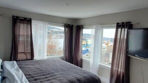 Een slaapkamer met een bed, een televisie en een raam met gordijnen.