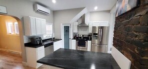 A modern kitchen with white cabinets, a black countertop, stainless steel appliances, and a brick accent wall. - Historic Signal Hill Escape. Hot tub/ocean view (St. John's)
