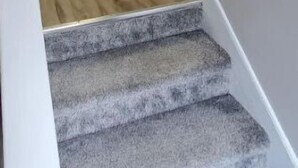 Een trap met beklede treden die leidt naar een ruimte met houten vloeren en witte deuren.
