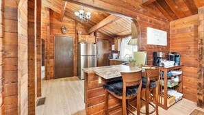 Una cabaña de madera rústica con una zona de cocina que incluye un refrigerador, estufa y asientos tipo barra.