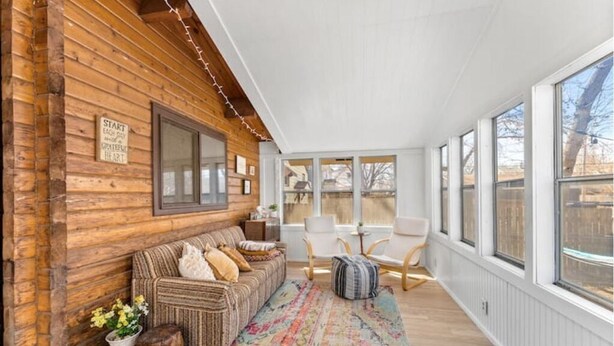 Un interior de cabaña acogedor, con pared de madera, un sofá, sillones y un ventanal grande.