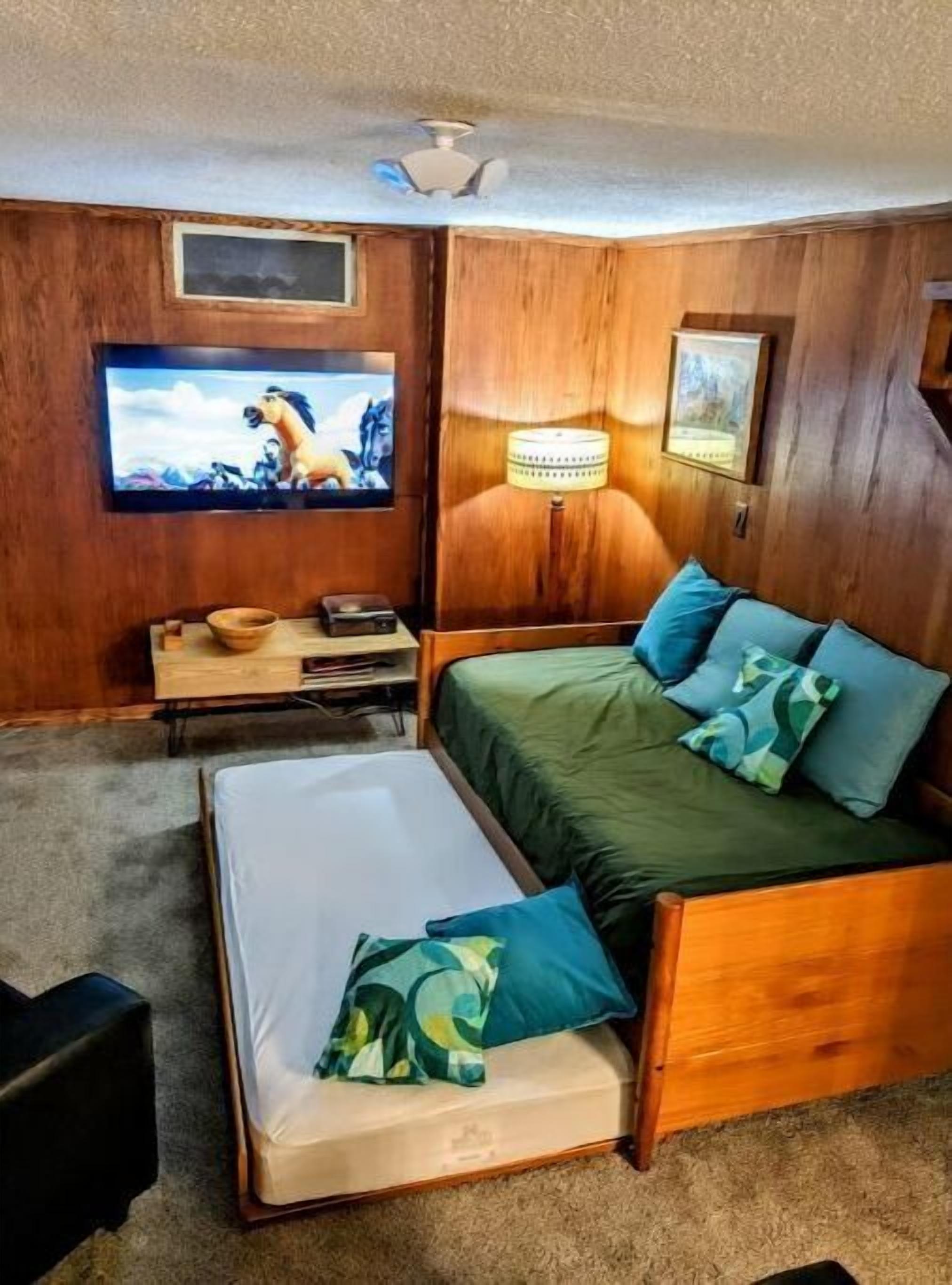Una habitación con una cama de madera, televisión, lámpara y una mesita con un bol y un control remoto.