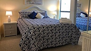 A bedroom with a bed, two bedside tables, a mirror, and a window with curtains.