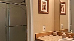 A bathroom with a glass shower enclosure, a toilet, a vanity with a sink, and framed pictures on the wall.