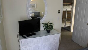 A bedroom with a television on a dresser, a potted plant, a bunk bed, and a white door.