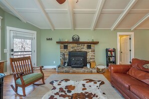 Un salon avec une cheminée en pierre, un fauteuil à bascule, un canapé en cuir et un tapis en peau de vache.