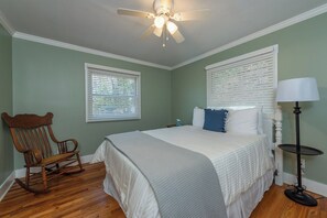 A bedroom with a bed, a rocking chair, a ceiling fan, and a lamp.