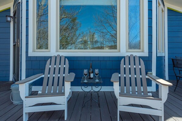 Two Adirondack chairs facing a window with a view of trees.