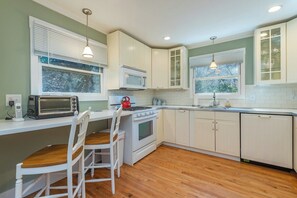 A kitchen with white cabinets, a stove, a microwave, and a window with blinds.