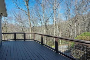 Une terrasse en bois avec une rambarde en métal, donnant sur une zone boisée.