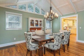 A dining area with a wooden table and patterned chairs, a chandelier, and a view into the kitchen.