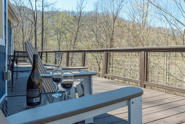 A wooden deck with a table and chairs, a bottle of wine, and a glass of wine.
