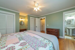 A bedroom with a bed, a ceiling fan, a dresser, a mirror, and a bathroom with a sink and mirror.