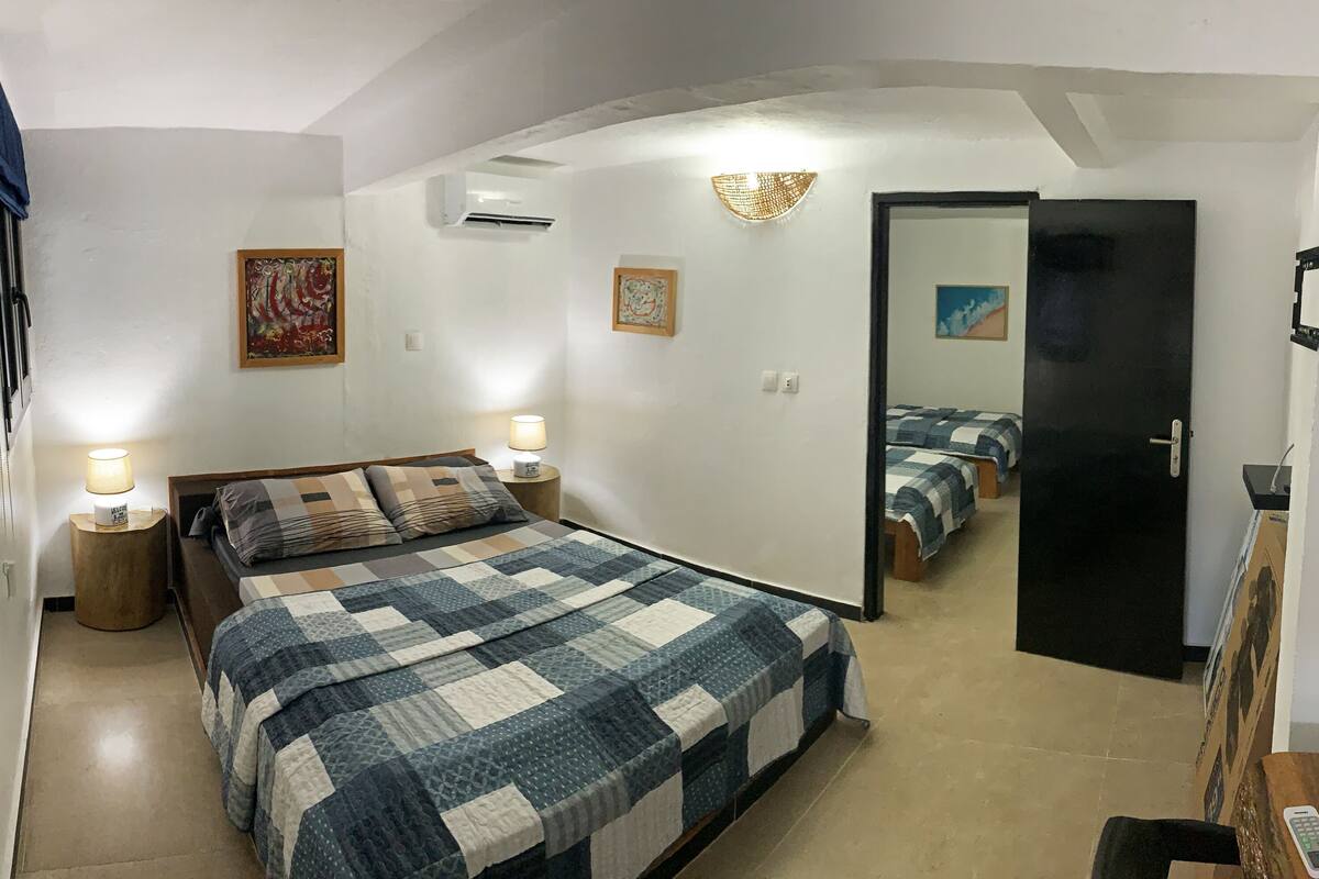 Un dormitorio con una cama grande, lámparas de noche, una puerta que da a otra habitación y un aire acondicionado de pared.