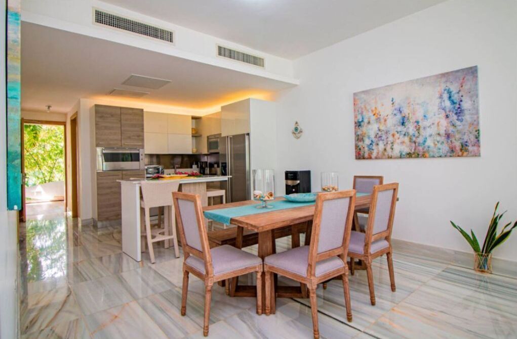 A modern kitchen with stainless steel appliances, a dining area with a wooden table and chairs, and a large abstract painting on the wall.