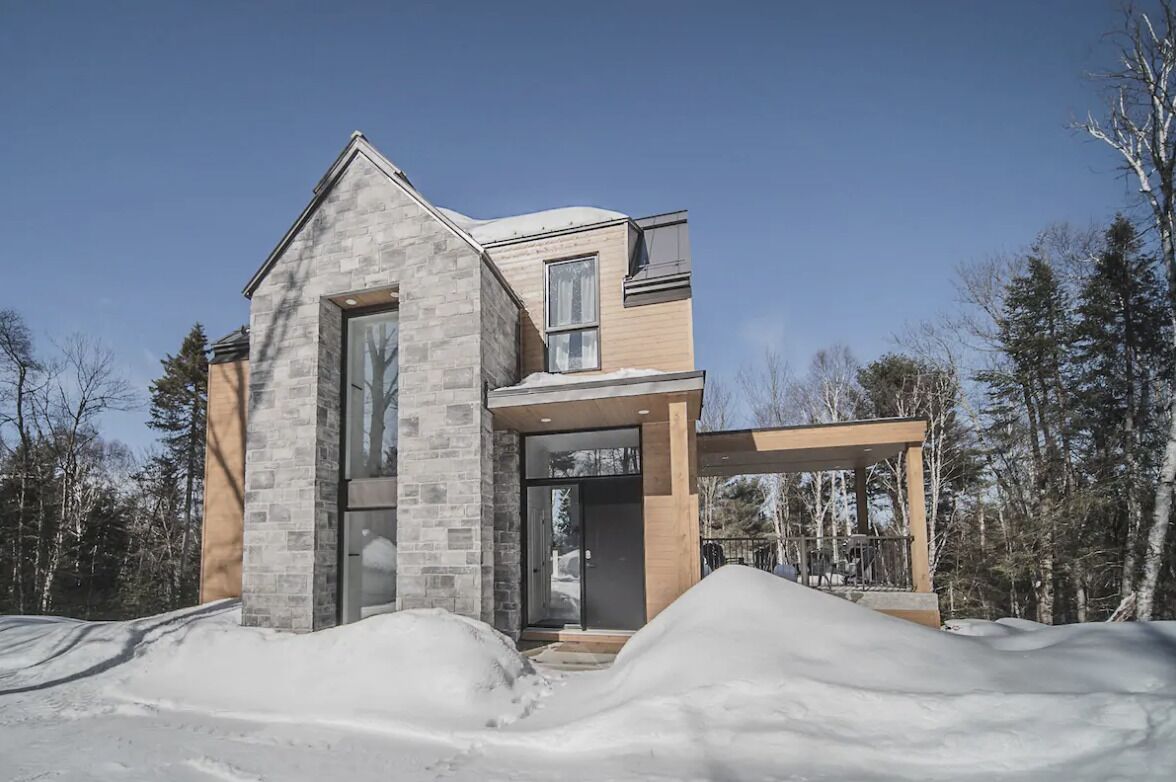A modern house with a stone facade, large windows, and a wooden porch.