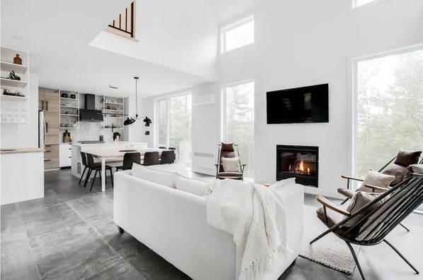 Una sala de estar moderna con un sofá blanco, una chimenea y un comedor con una cocina al fondo.