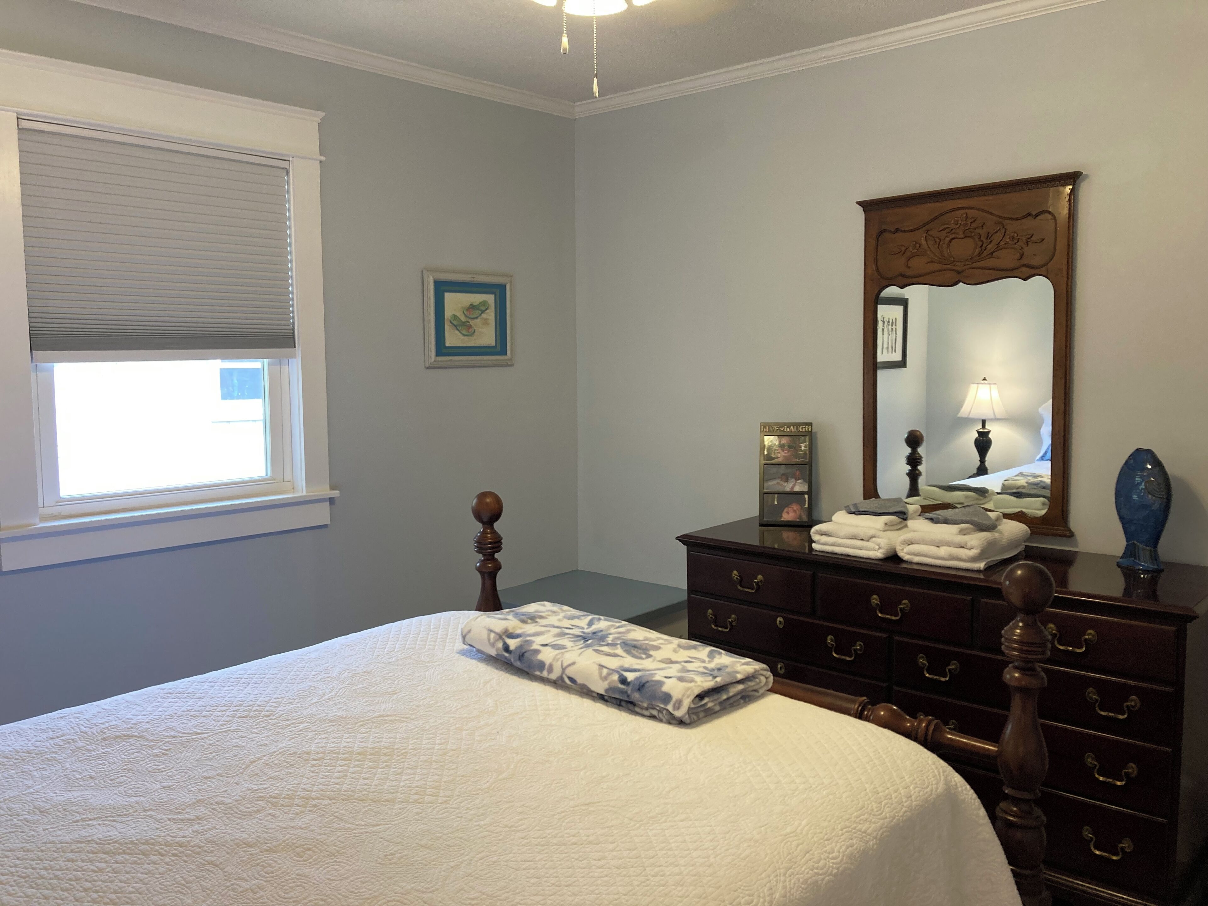 A bedroom with a bed, a dresser, a mirror, and a window with blinds.
