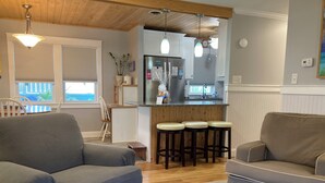 A living room with a grey sofa, a brown sofa, and a kitchen area with a refrigerator, sink, and bar stools. - Pet-Friendly OBX Retreat - 3BR/2BA -  Private Beach Parking MP6 Kill Devil Hills (Kill Devil Hills)
