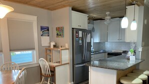 A modern kitchen with a central island, white cabinetry, and a dining area with a wooden table and chairs. - Pet-Friendly OBX Retreat - 3BR/2BA -  Private Beach Parking MP6 Kill Devil Hills (Kill Devil Hills)