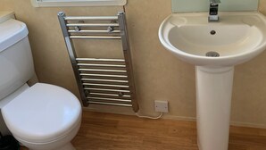 Un baño con inodoro blanco, toallero cromado y lavamanos pedestal blanco.