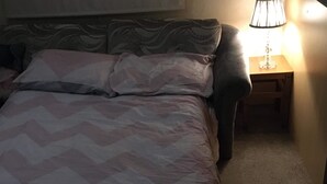 Una cama con ropa de cama estampada, una mesita de noche con lámpara y un panel decorativo en la pared.