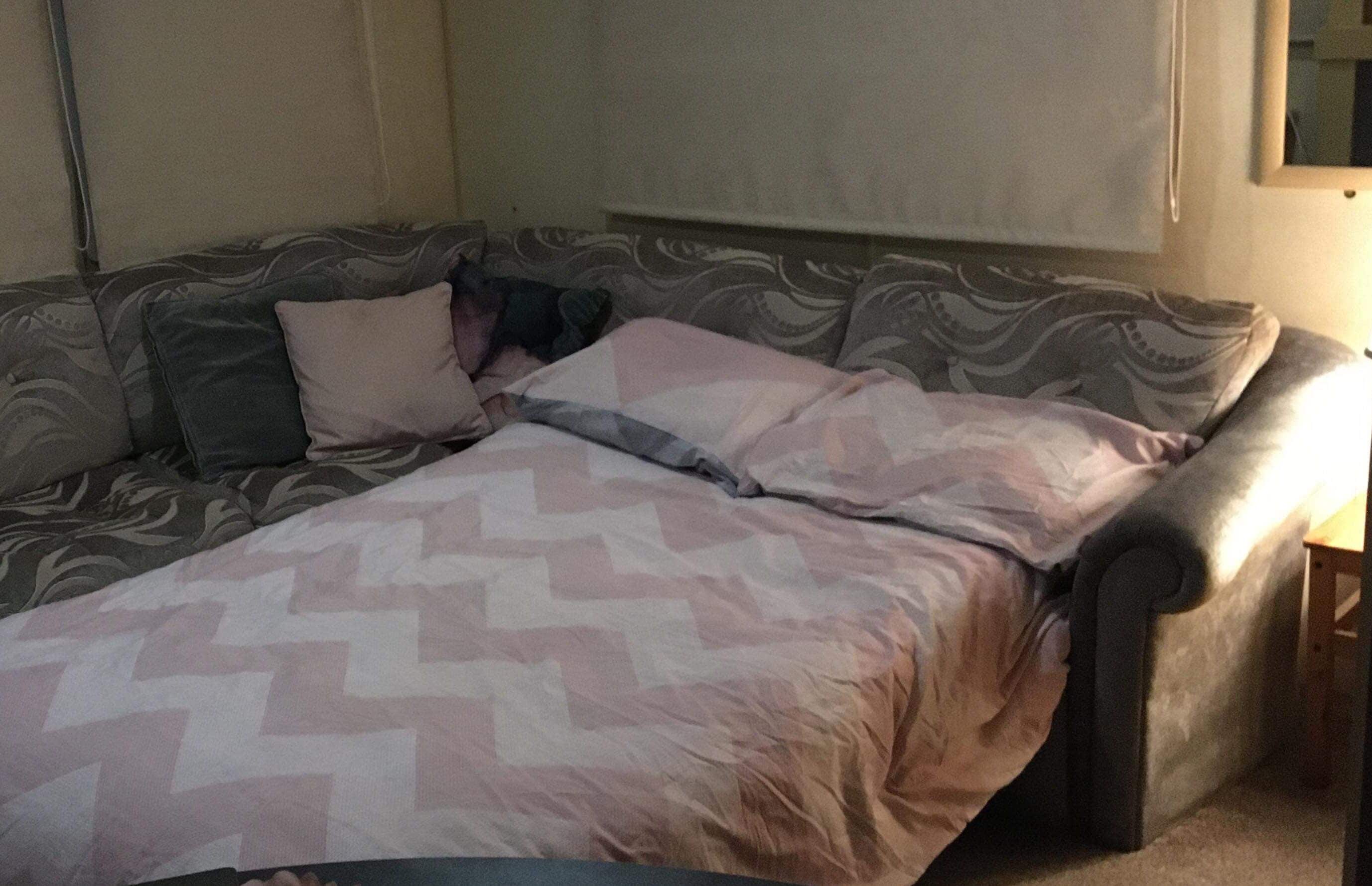 Een kamer met een slaapbank, een bedekker met patroon en een klein houten tafeltje.