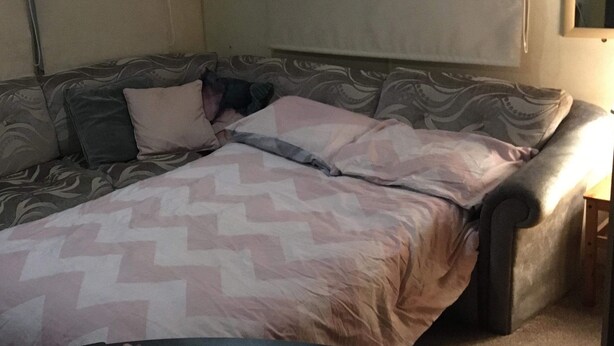 Una habitación con sofá cama, una manta estampada y una pequeña mesa de madera.