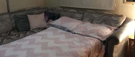 A room with a sofa bed, a patterned blanket, and a small wooden table.