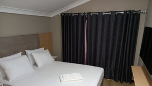 A neatly made bed with white linens, a wooden headboard, and a small bedside table. - Acacus Hotel (Kigali)