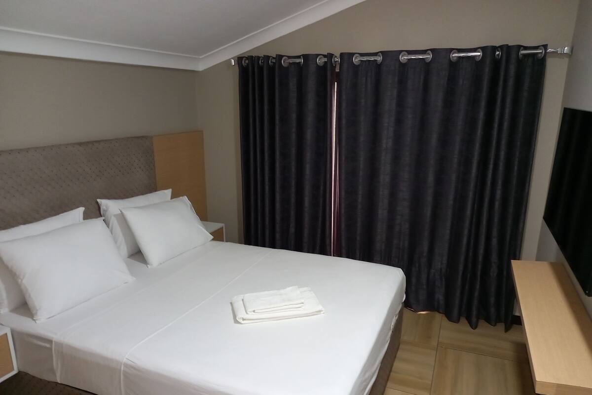 A neatly made bed with white linens, a wooden headboard, and a small bedside table.
