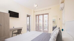 Ein Schlafzimmer mit einem Bett, einem Schreibtisch, einem Stuhl, einem Fernseher und einem Fenster mit Vorhängen.