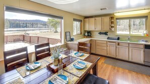 A spacious kitchen with wooden cabinets, a dining area with a table set for four, and large windows offering a view of a forested area. - Hike, Bike & Boat: Cabin w/ Dock on Seeley Lake! (Seeley Lake)