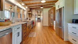 A kitchen with wooden floors, white cabinets, stainless steel appliances, and pendant lighting. - Spacious Alabama Retreat - Deck, Grill & Fire Pit! (Crane Hill)