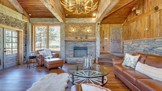 A spacious living room with a stone fireplace, leather furniture, and a chandelier. - Spacious Alabama Retreat - Deck, Grill & Fire Pit! (Crane Hill)