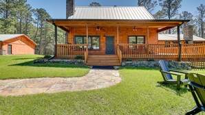 A wooden cabin with a stone pathway leading to the entrance, surrounded by a grassy yard and trees. - Spacious Alabama Retreat - Deck, Grill & Fire Pit! (Crane Hill)