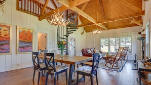 A spacious dining area with a wooden table and chairs, a chandelier, and a staircase leading to an upper level. - Spacious Alabama Retreat - Deck, Grill & Fire Pit! (Crane Hill)