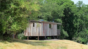 A rustic wooden cabin with a chimney, surrounded by dense forest.