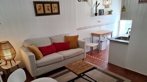 A living room with a sofa, a coffee table, a lamp, and a chair. There is a kitchen area with a sink and a dining table. - Raoret House in the Old Town (Villajoyosa)