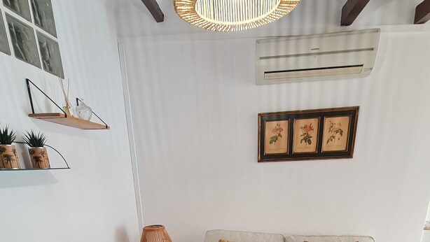 A living room with a white sofa, two cushions, a round chair, a wooden coffee table, a floor lamp, and wall-mounted shelves with decorative items. - Raoret House in the Old Town (Villajoyosa)