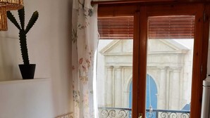 A small kitchen with a dining table and chair, a potted cactus, and a view of a building through a wooden door with a metal gate. - Raoret House in the Old Town (Villajoyosa)