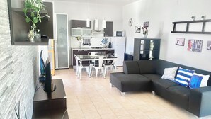 Ein modernes Wohnzimmer mit einem dunklen Sofa, einem Esstisch und einer Küche im Hintergrund.