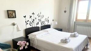 Ein ordentlich eingerichtetes Hotelzimmer mit Bett, Nachttischen, einer Lampe, einer Vase mit Blumen und einem Fenster mit Vorhängen.