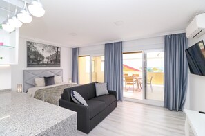 A modern hotel room with a bed, a sofa, a dining area, and a balcony with curtains.