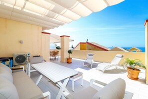 Une terrasse sur le toit avec une table, des chaises, un ventilateur et une plante en pot.