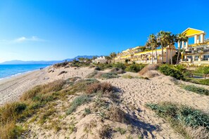 Un complexe hôtelier de bord de mer doté d’une plage de sable, de palmiers et d’un bâtiment aux touches de couleur jaune.