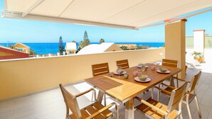 A dining area with a table set for four, chairs, and a view of the sea.