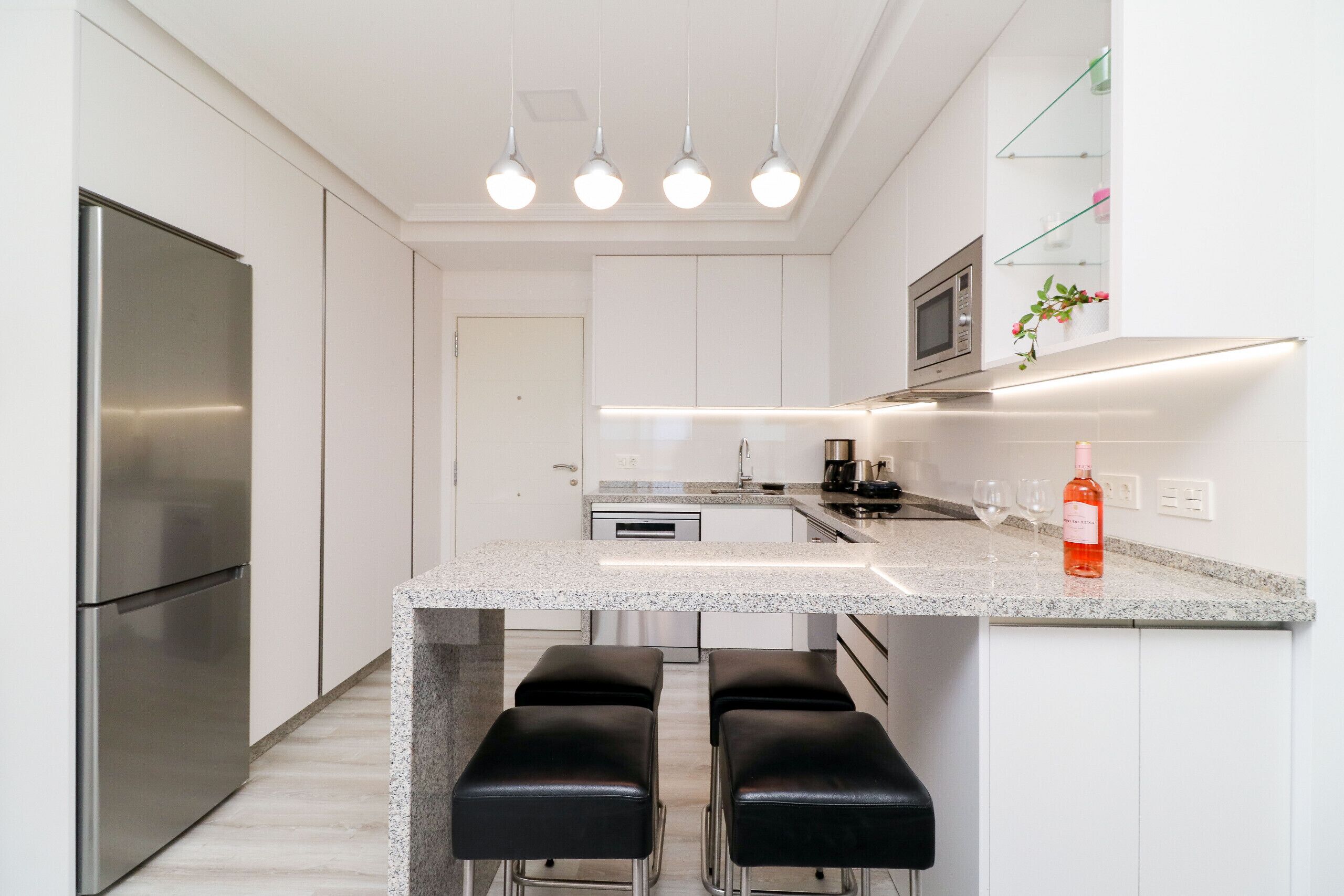 A modern kitchen with a stainless steel refrigerator, a granite countertop, and a bar area with stools.
