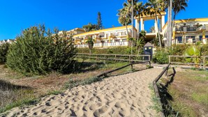 A sandy pathway leading to a hotel with multiple balconies and palm trees.
